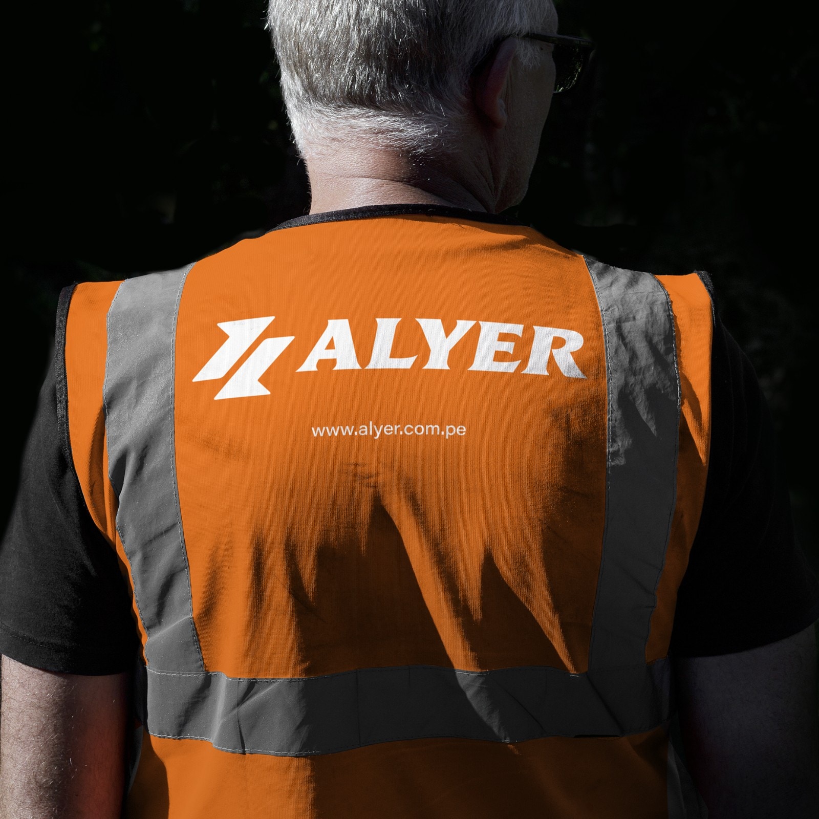 Un trabajador de espaldas con el chaleco reflectivo de Alyer y la dirección web bajo el logotipo